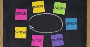 Days of week presented as a cycle with colorful sticky notes and white chalk on blackboard
