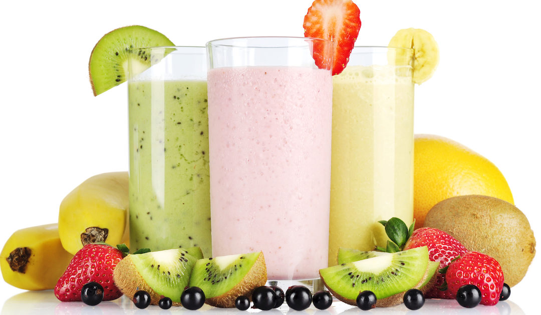 Three smoothies with varying fruit surrounding their glasses