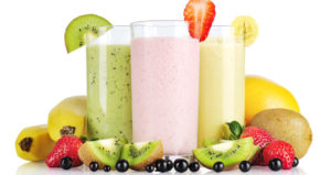 Three smoothies with varying fruit surrounding their glasses